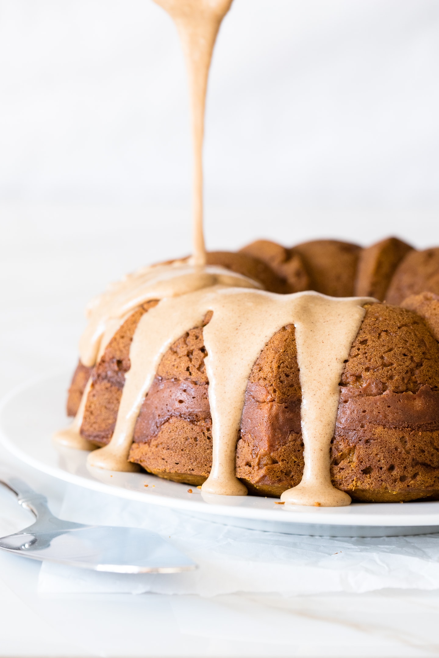 Front-facing view of brown sugar icing being poured over a pumpkin bundt cake.
