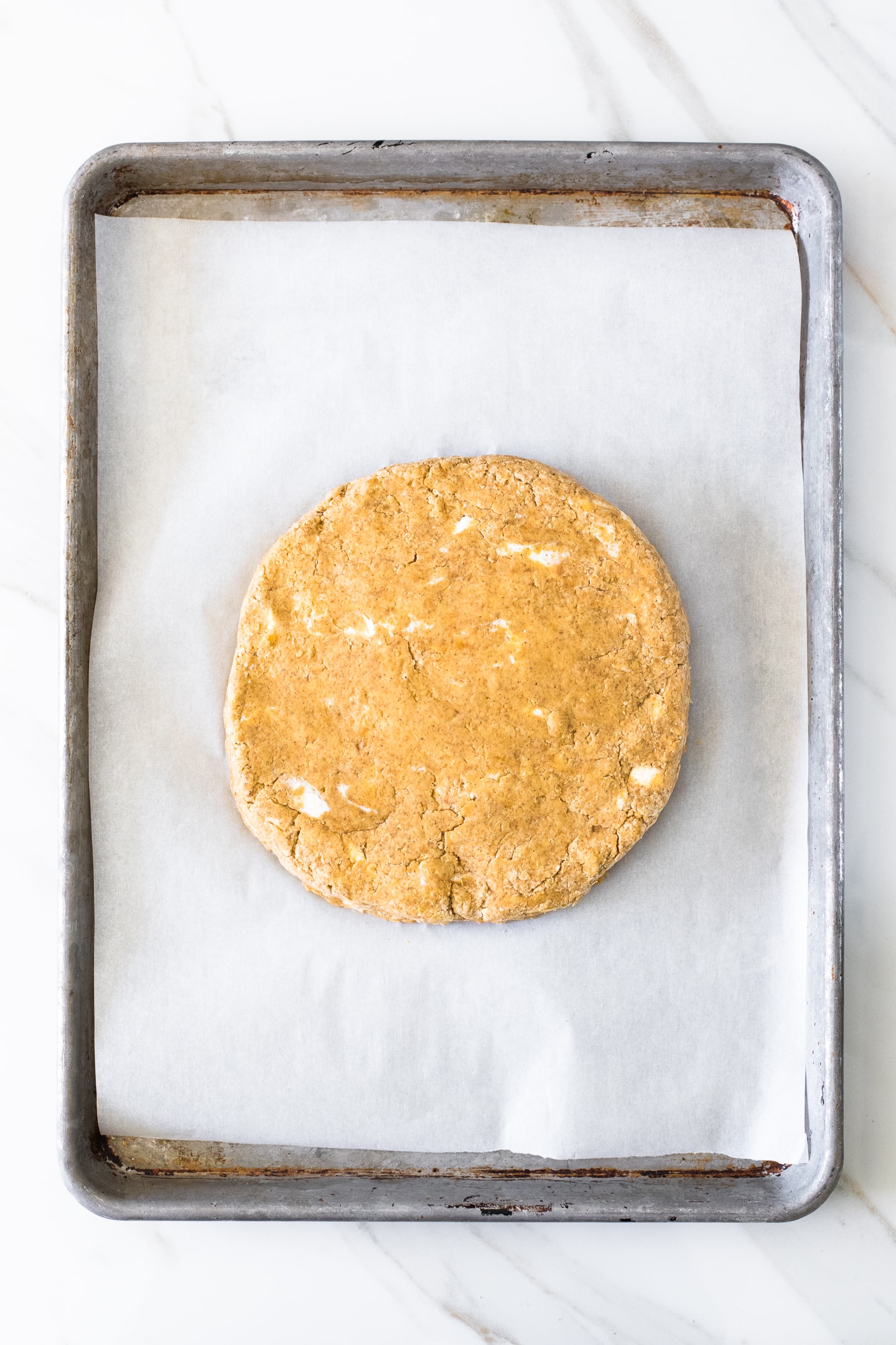 Overhead view of pumpkin scone dough shaped into a disc and placed on a parchment-lined baking tray.