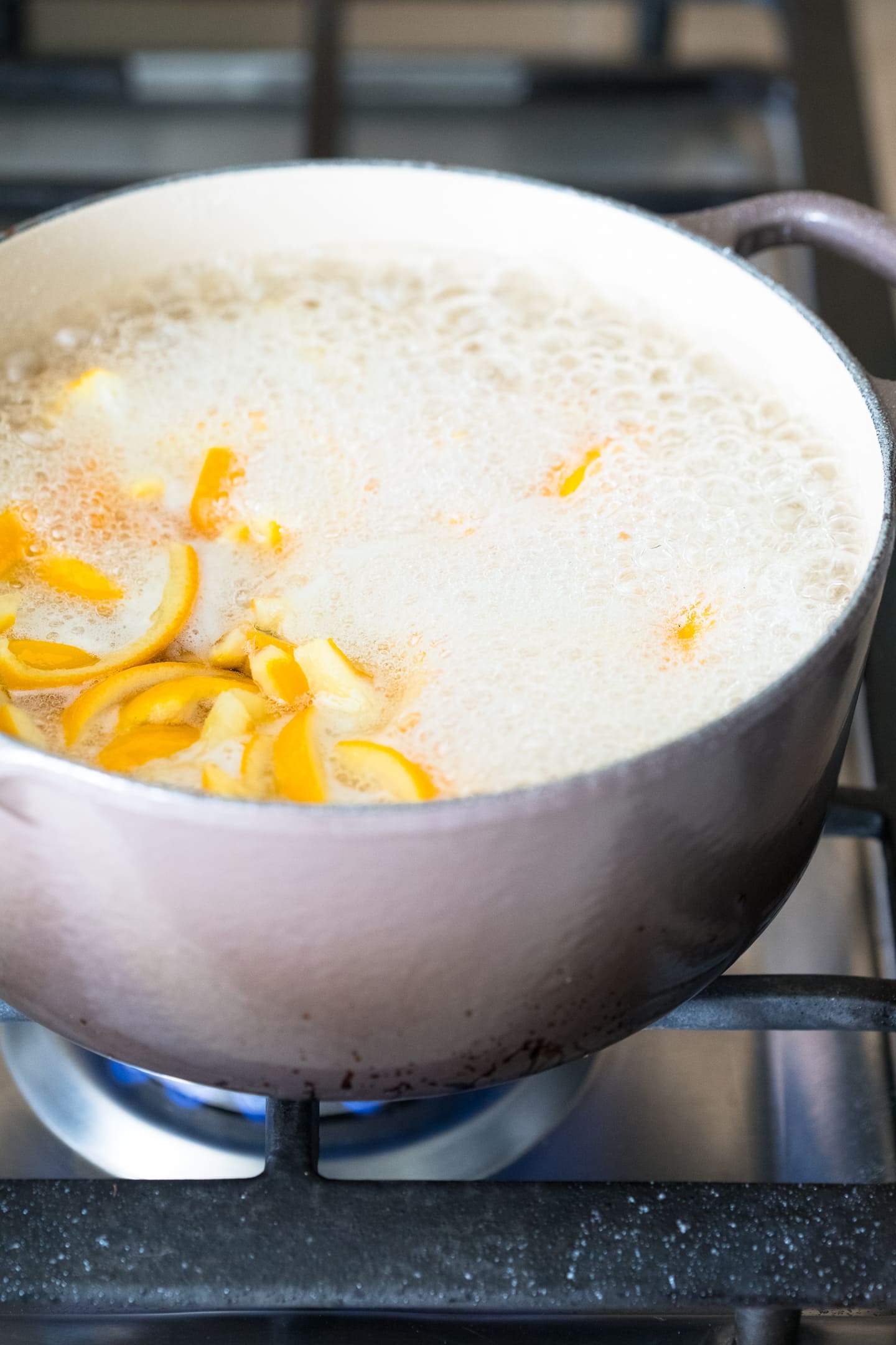 Angled view of orange peels simmering in sugar syrup in a pot on the stove.