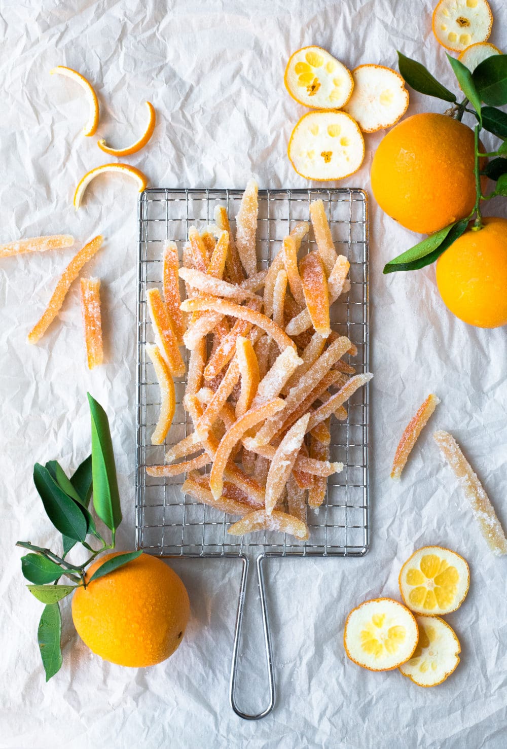 Overhead view of strips of candied orange peel on a safety grater, surrounded by more oranges and peel cuttings.