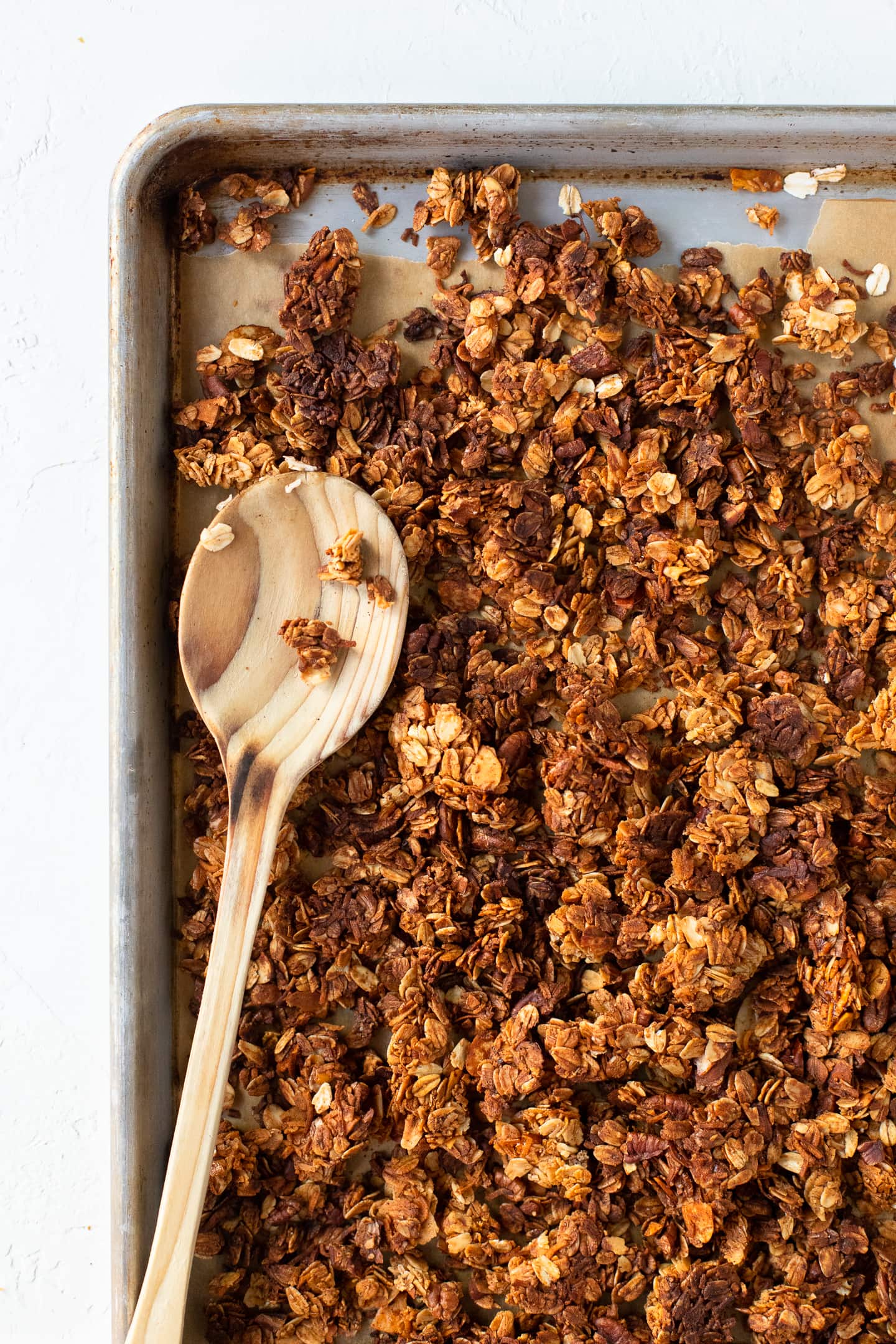 Overhead view of baked granola on a baking sheet, with a wooden spoon laying across the top.