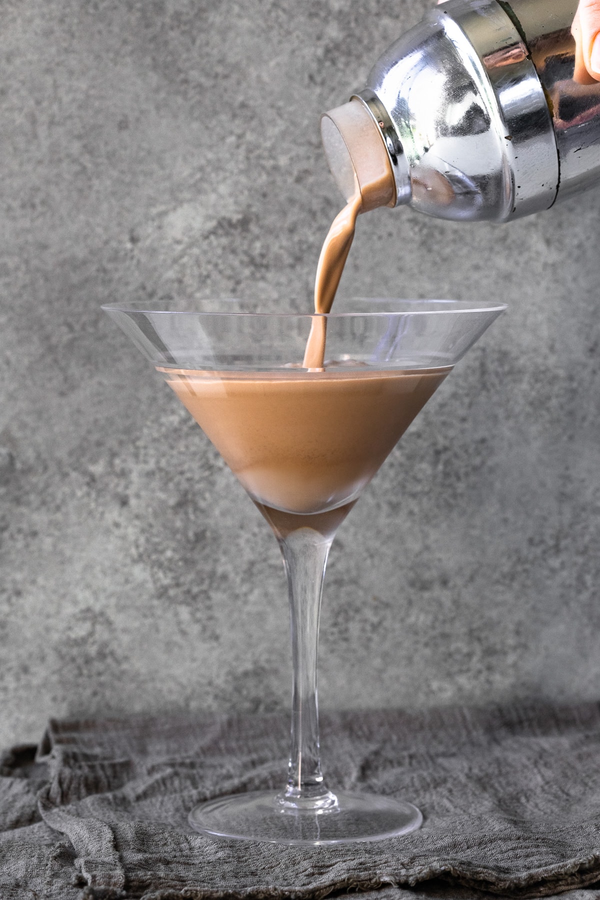 Espresso martini with Irish cream being poured from a cocktail shaker into a glass.