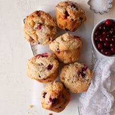 Muffins arranged on a safety grater alongside bowls of fresh cranberries and sparkling sugar.
