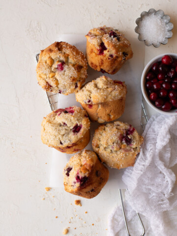Muffins arranged on a safety grater alongside bowls of fresh cranberries and sparkling sugar.