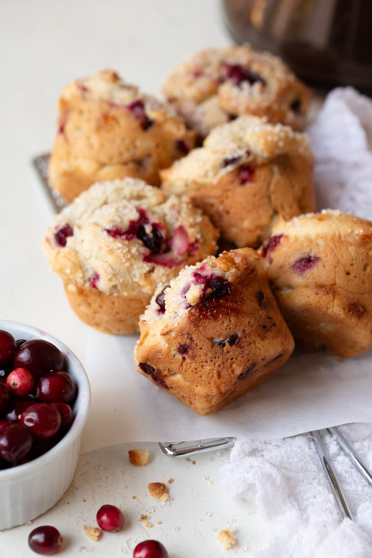 Six cranberry white chocolate muffins with a bowl of cranberries to the side.
