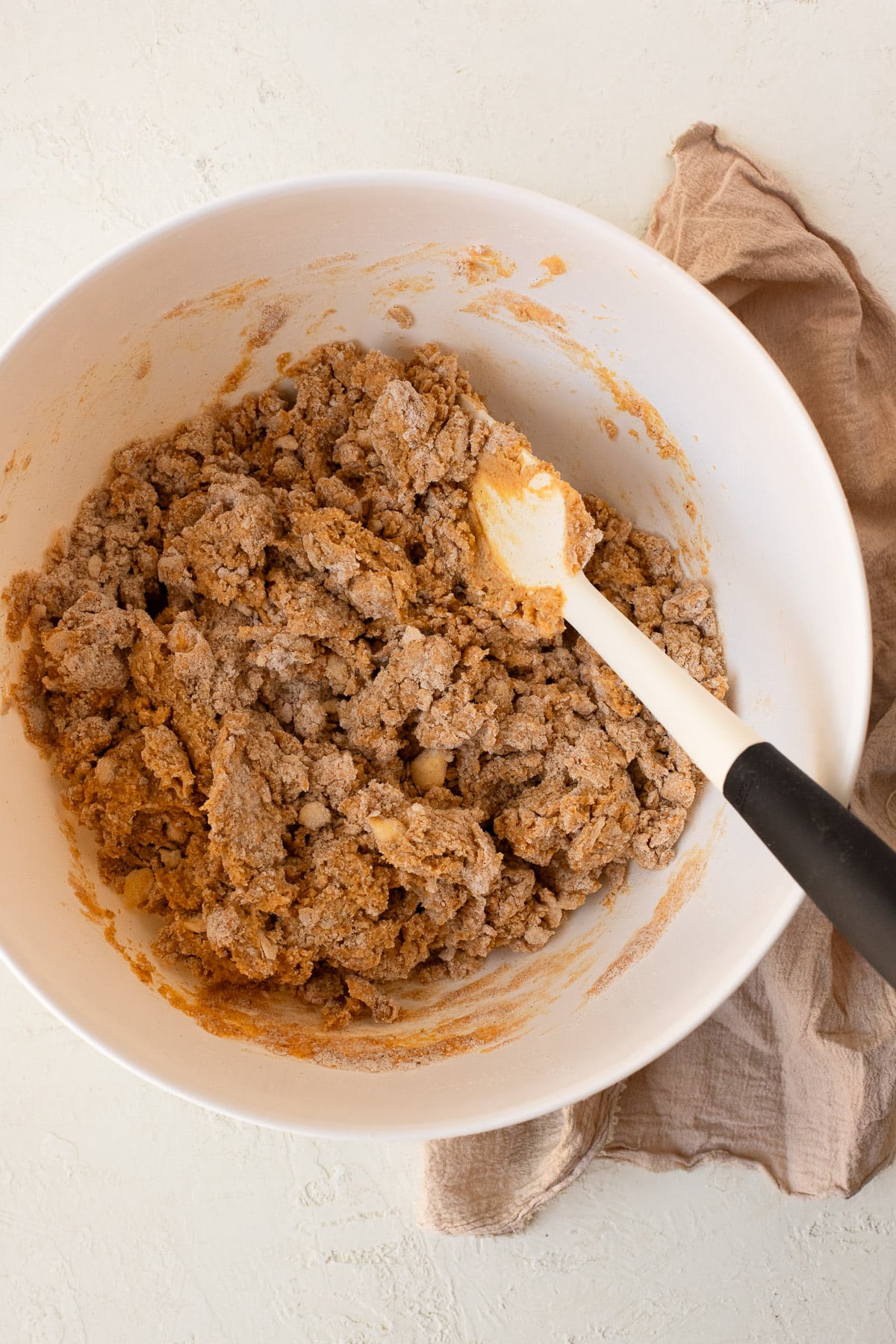 Pumpkin scone dough being mixed with a rubber spatula in a bowl.