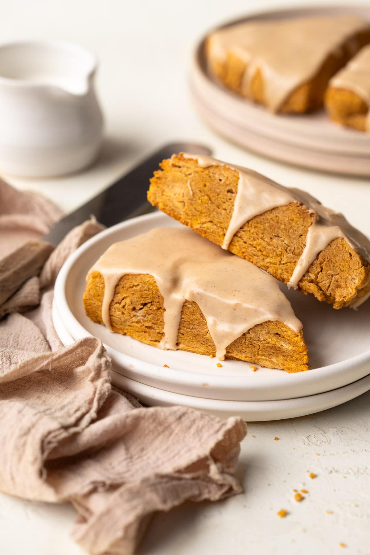 Two pumpkin scones topped with maple glaze on stacked white plates.