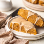 Two pumpkin scones topped with maple glaze on stacked white plates.
