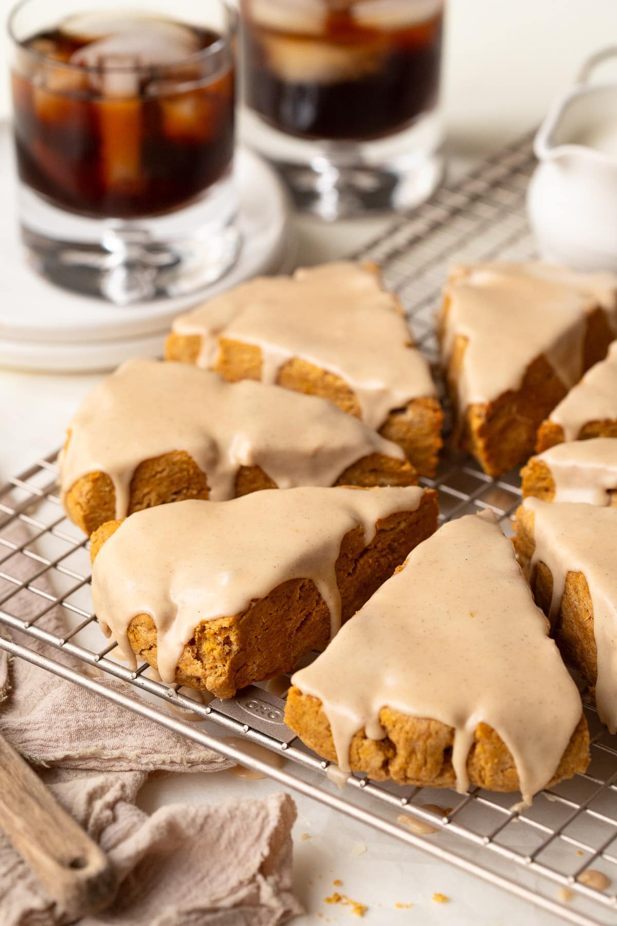Pumpkin scones topped with glaze on a wire rack, with iced coffee in the background.