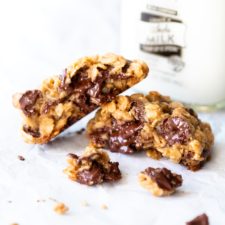 Front-facing view of a Gluten-Free Oatmeal Chocolate Chip Cookie, warm from the oven and broken in half, in front of a bottle of Rosa Brothers milk.
