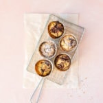 Overhead recipe image of Marble Financiers baked in muffin cups, placed on a safety grater over a crinkled sheet of parchment and a blush pink backdrop.