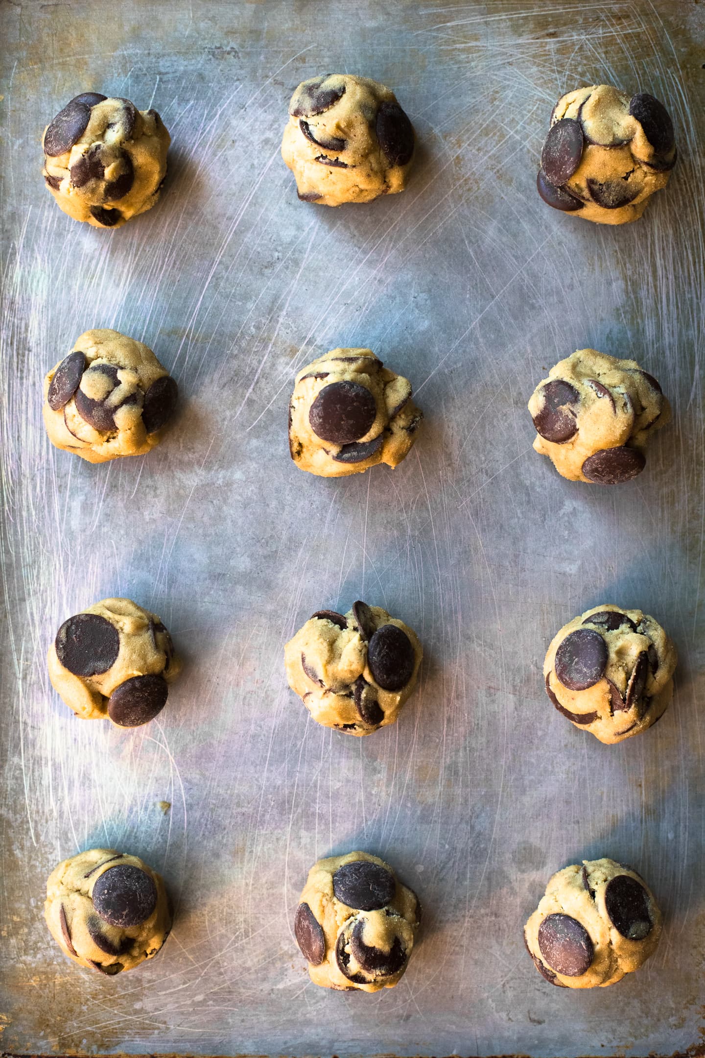 Overhead view of gluten-free chocolate chip cookie dough rolled into balls and arranged on a baking sheet.