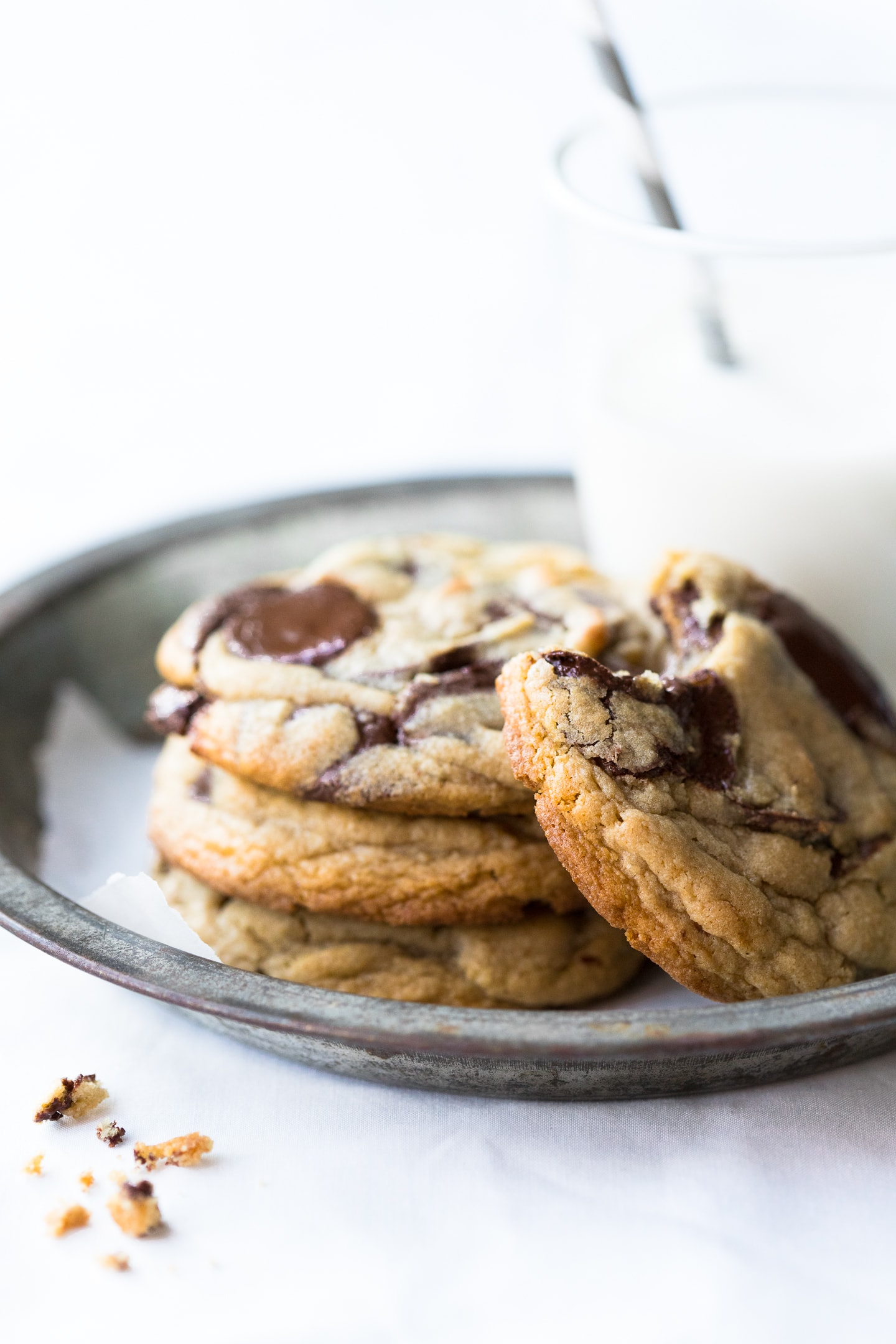 Front-angled view of gluten-free chocolate chip cookies stacked on a tin pie plate next to a glass of milk.