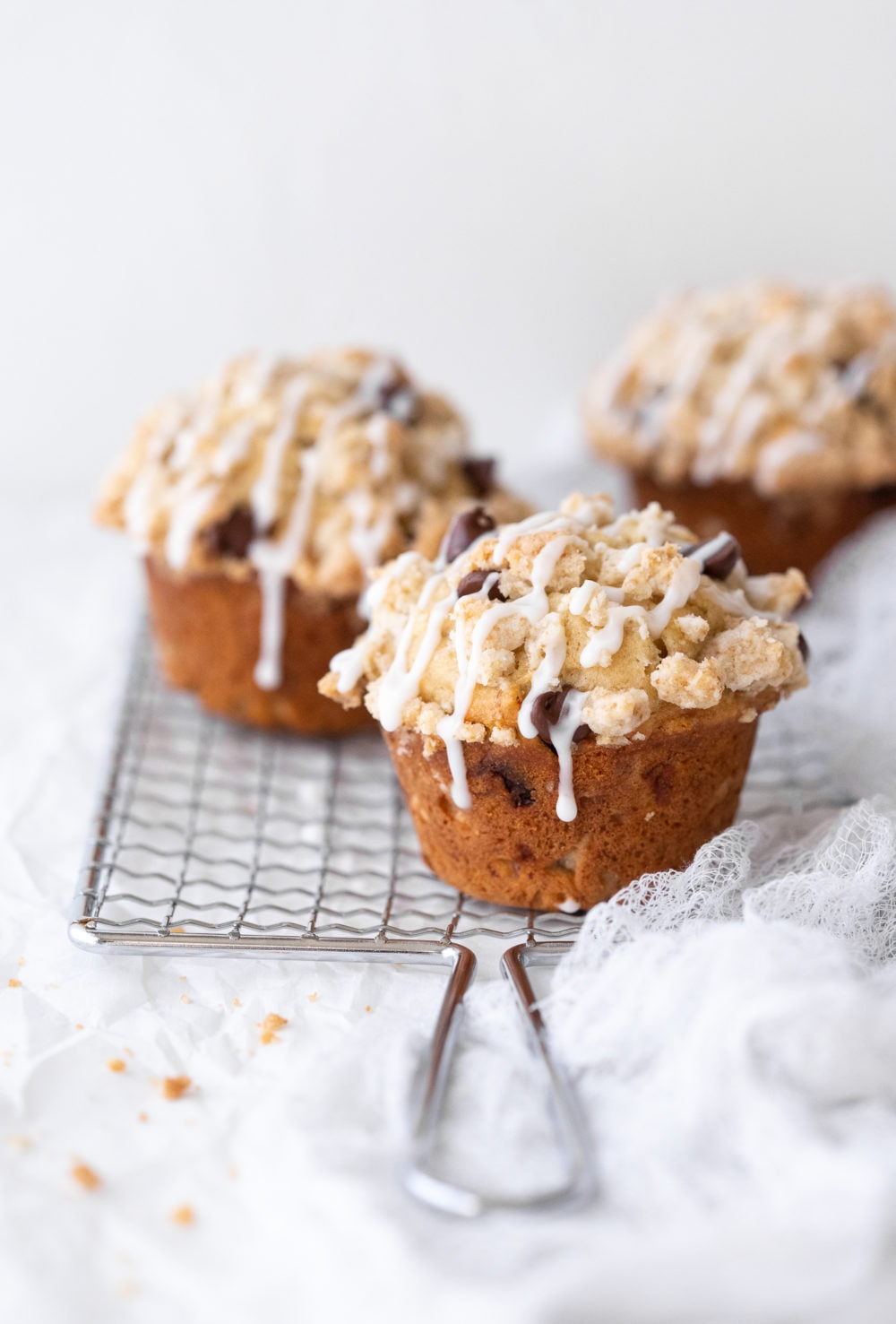 Three gluten-free banana chocolate chip muffins placed on a safety grater over a white backdrop.