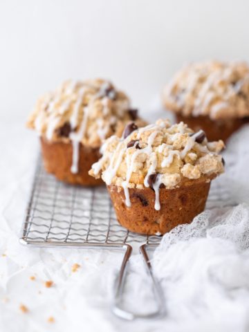 Three gluten-free banana chocolate chip muffins placed on a safety grater over a white backdrop.