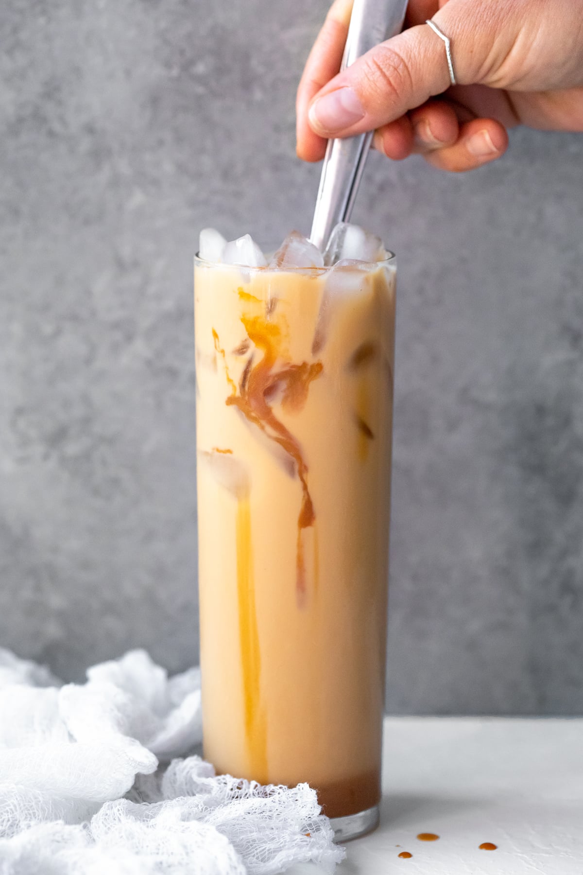 Carmel being stirred into an iced coffee against a grey backdrop.