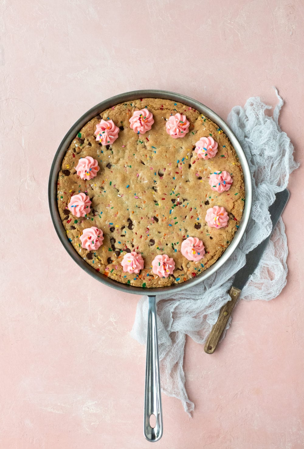 Overhead view of a chocolate chip cookie cake baked in a skillet, with a linen and serving spatula to the side.