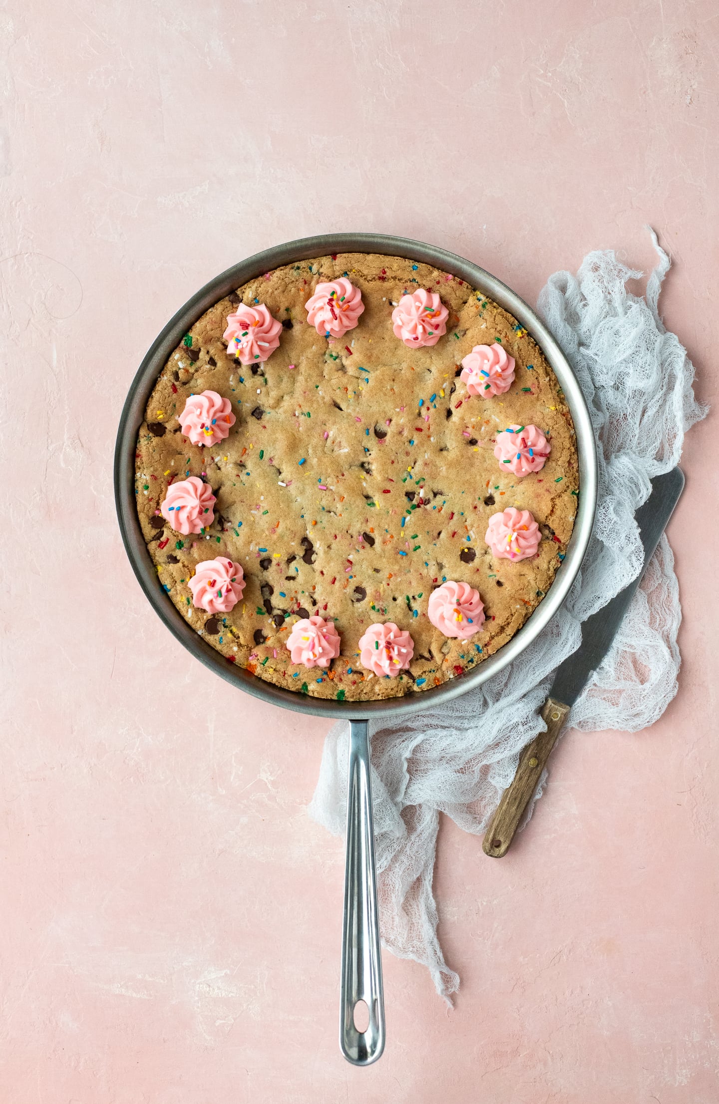 Overhead view of a chocolate chip cookie cake baked in a skillet, with a linen and serving spatula to the side.