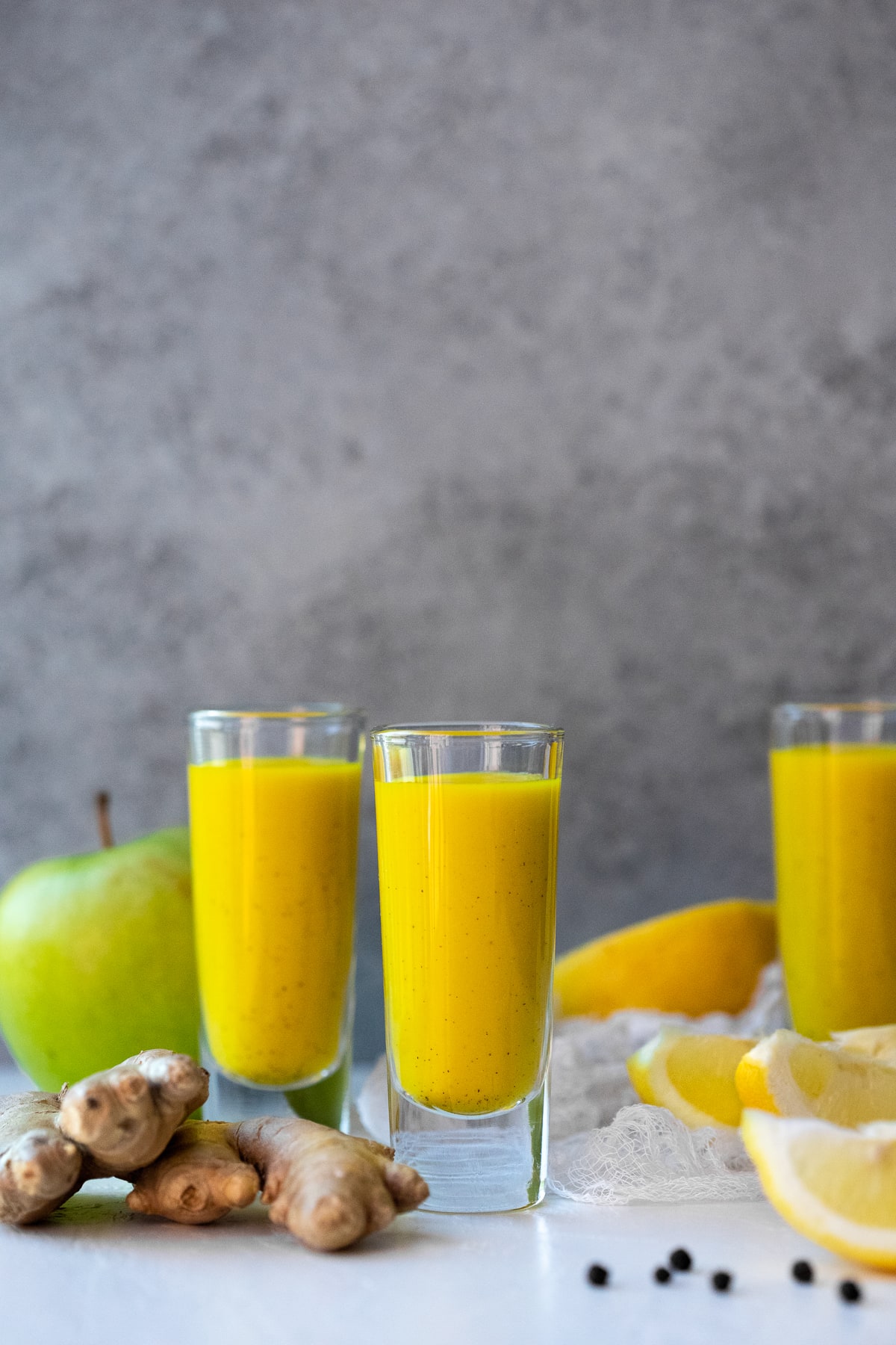 Juice shots surrounded by ingredients against a grey background.