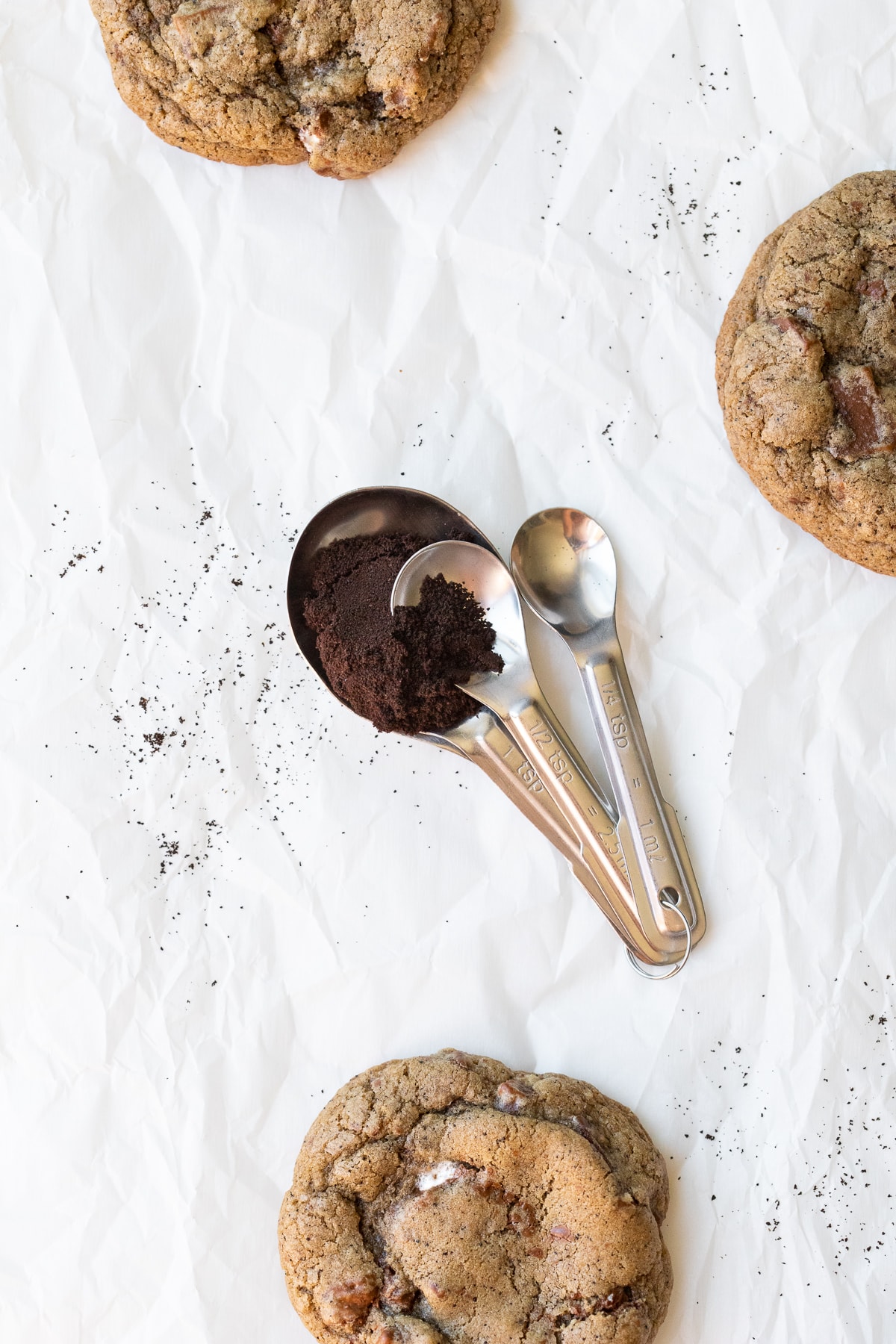 Teaspoon set being used to measure espresso powder, surrounded by cookies.