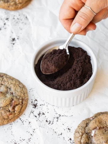 Hand spooning espresso powder out of a ramekin, surrounded by cookies.