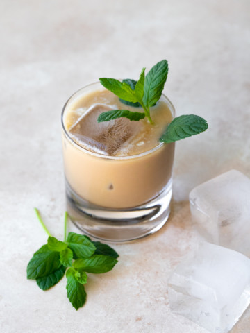 Angled view of a single iced coffee, with mint springs and ice cubes in the foreground.