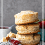 Front-facing view of 3 biscuits stacked atop each other, with a spoonful of jam in for foreground and a basket of strawberries in the background. Text overlay has recipe name and description.