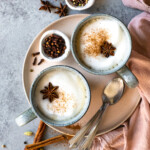Lattes garnished with star anise and cinnamon, with extra spice and honey in the background.