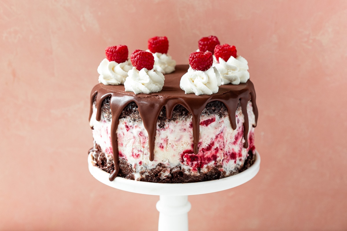 Ice cream cake on a cake stand against a pink backdrop.