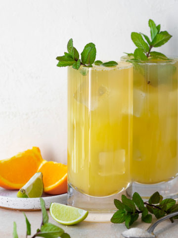 Two orange mojitos served in highball glasses, garnished with fresh mint sprigs.