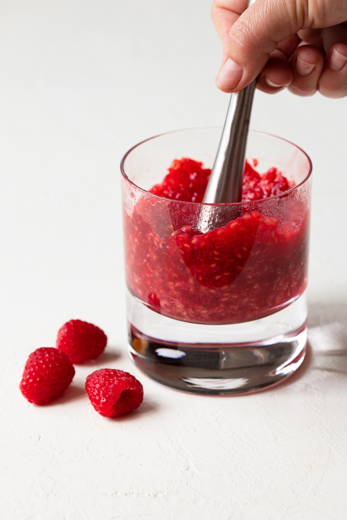 Raspberries being muddled in a glass.
