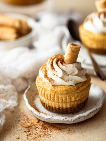Mini pumpkin cheesecake topped with whipped cream, on a plate.