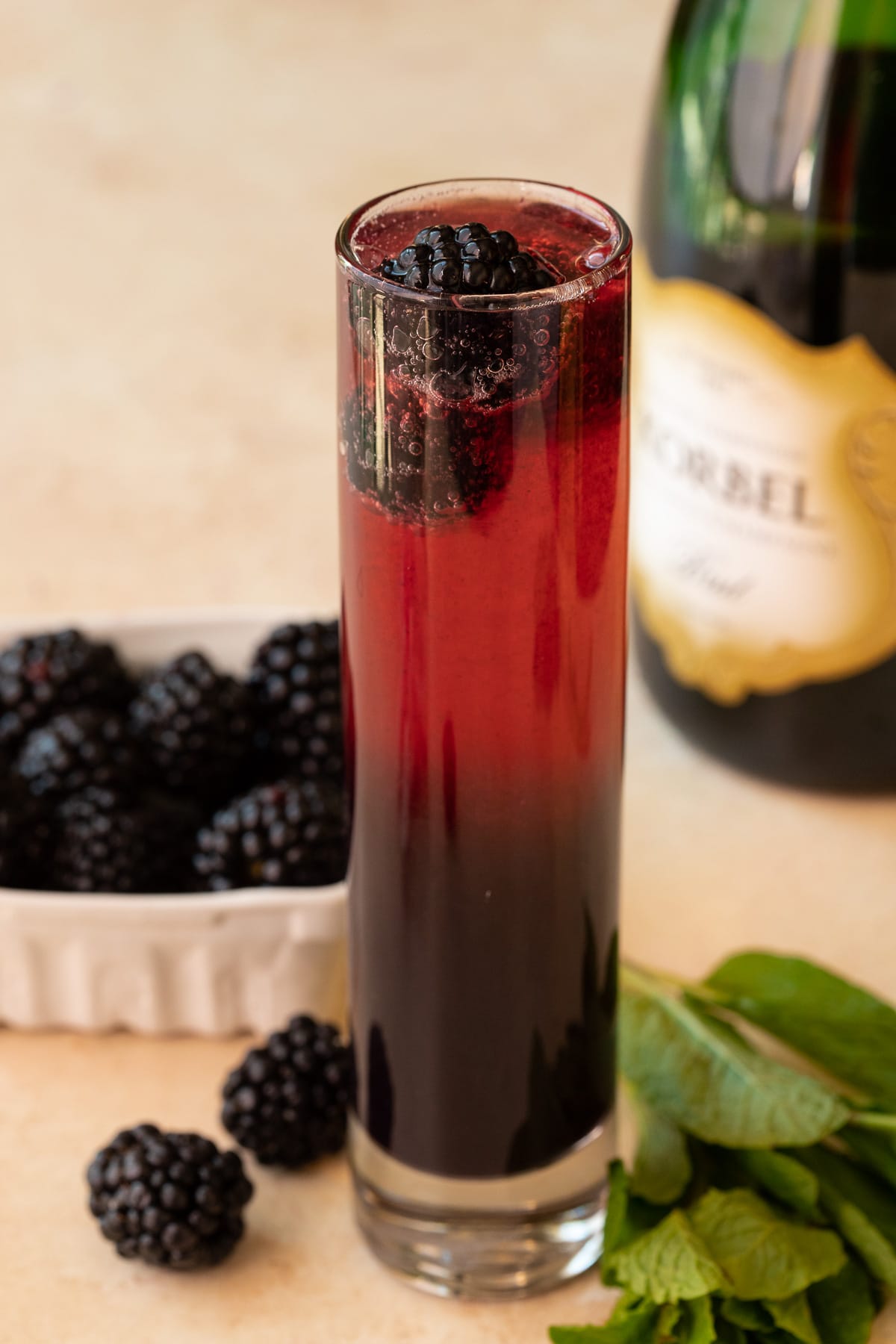 A mimosa garnished with blackberries, with berries and mint in the background.