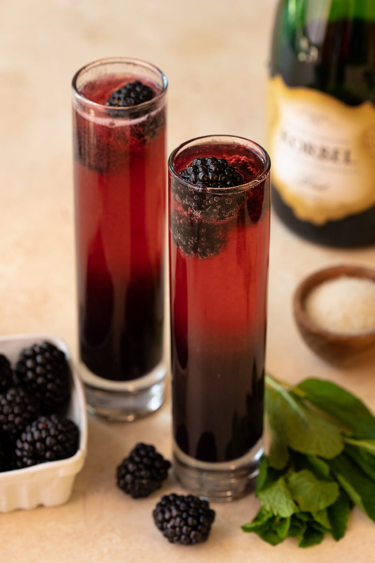 Two mimosas in champagne glasses garnished with fresh blackberries.