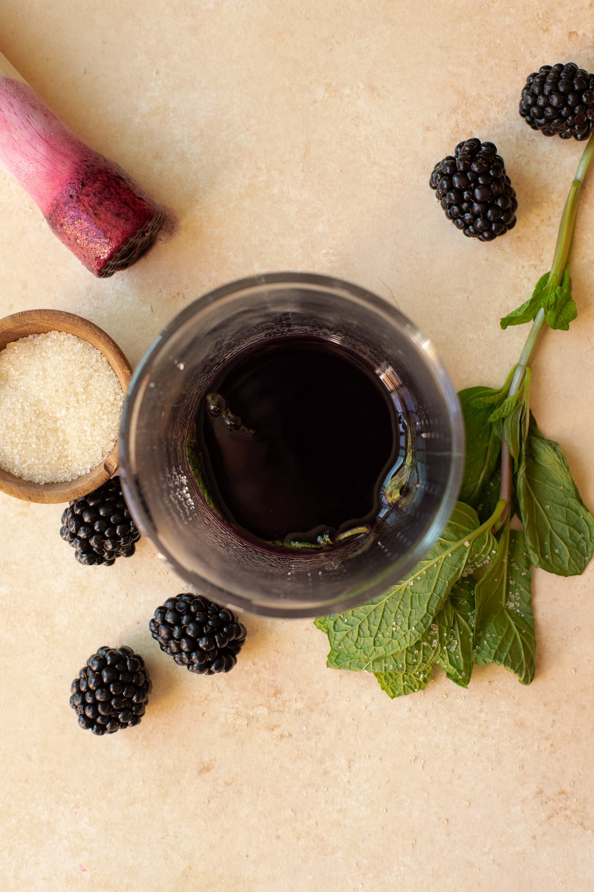 Blackberry juice in a glass with a muddler, fresh mint, and sugar.