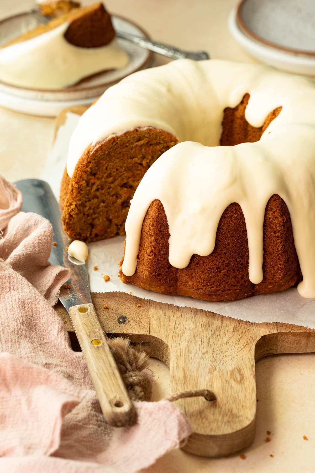Bundt cake topped with frosting, with a slice removed, on a wooden board.
