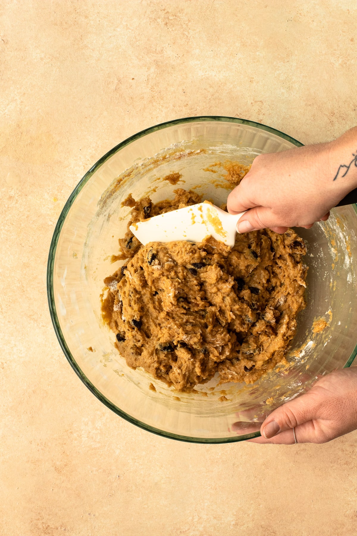 Raisin cinnamon roll dough being mixed with a spatula in a glass bowl.
