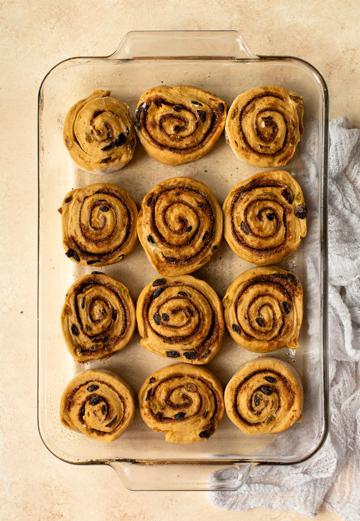 Sliced cinnamon rolls arranged in a glass baking dish to rise.