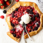 A sliced galette topped with a scoop of ice cream and surrounded by fresh berries.