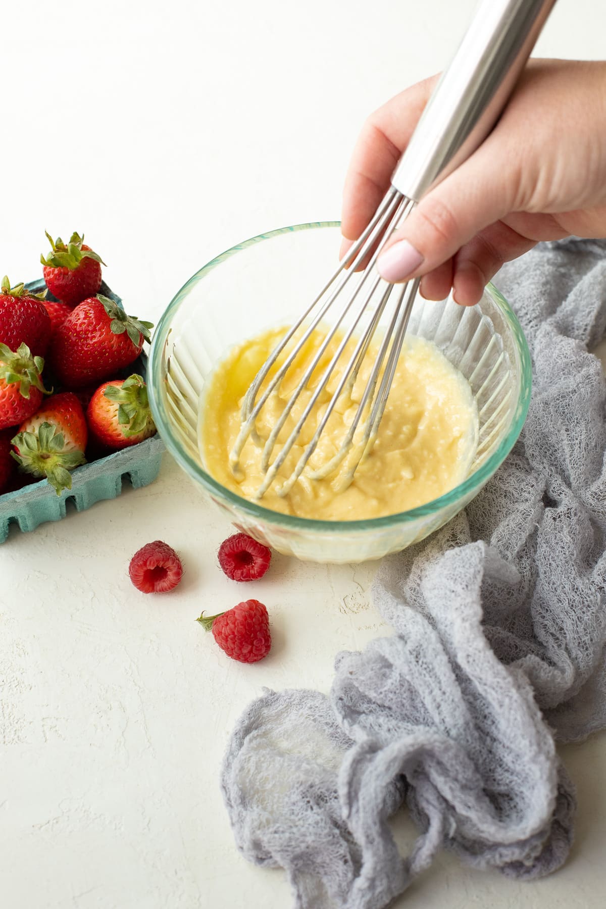 Cream cheese filling being whisked together in a small bowl, with berries in the background.