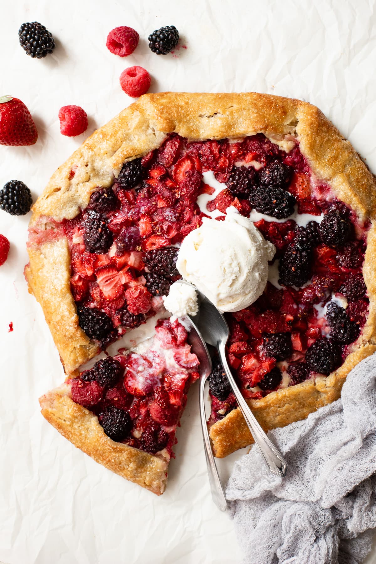 A sliced galette topped with a scoop of ice cream and surrounded by fresh berries.