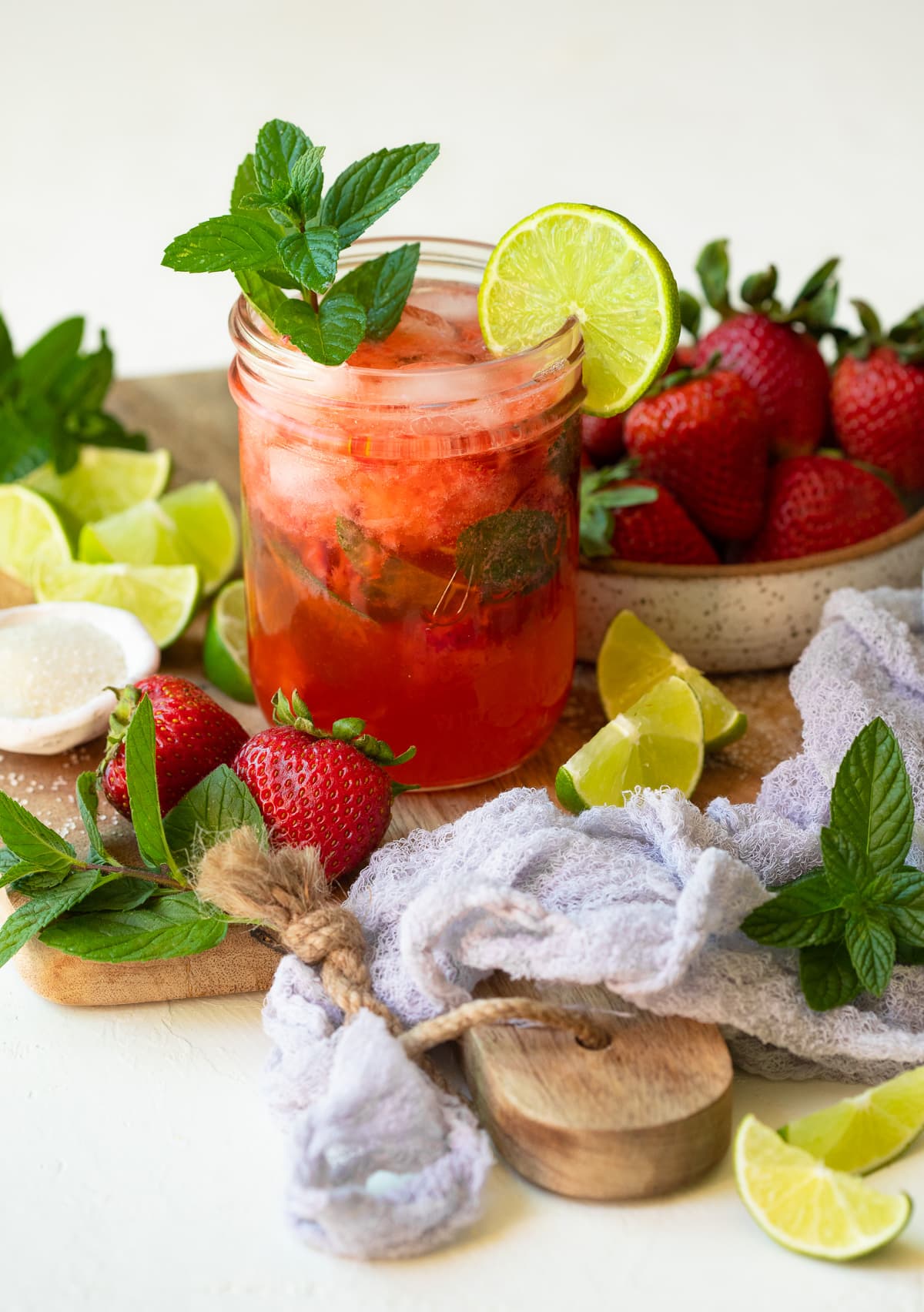 A Strawberry Mojito served in a mason jar and garnished with lime and mint on a wooden board.