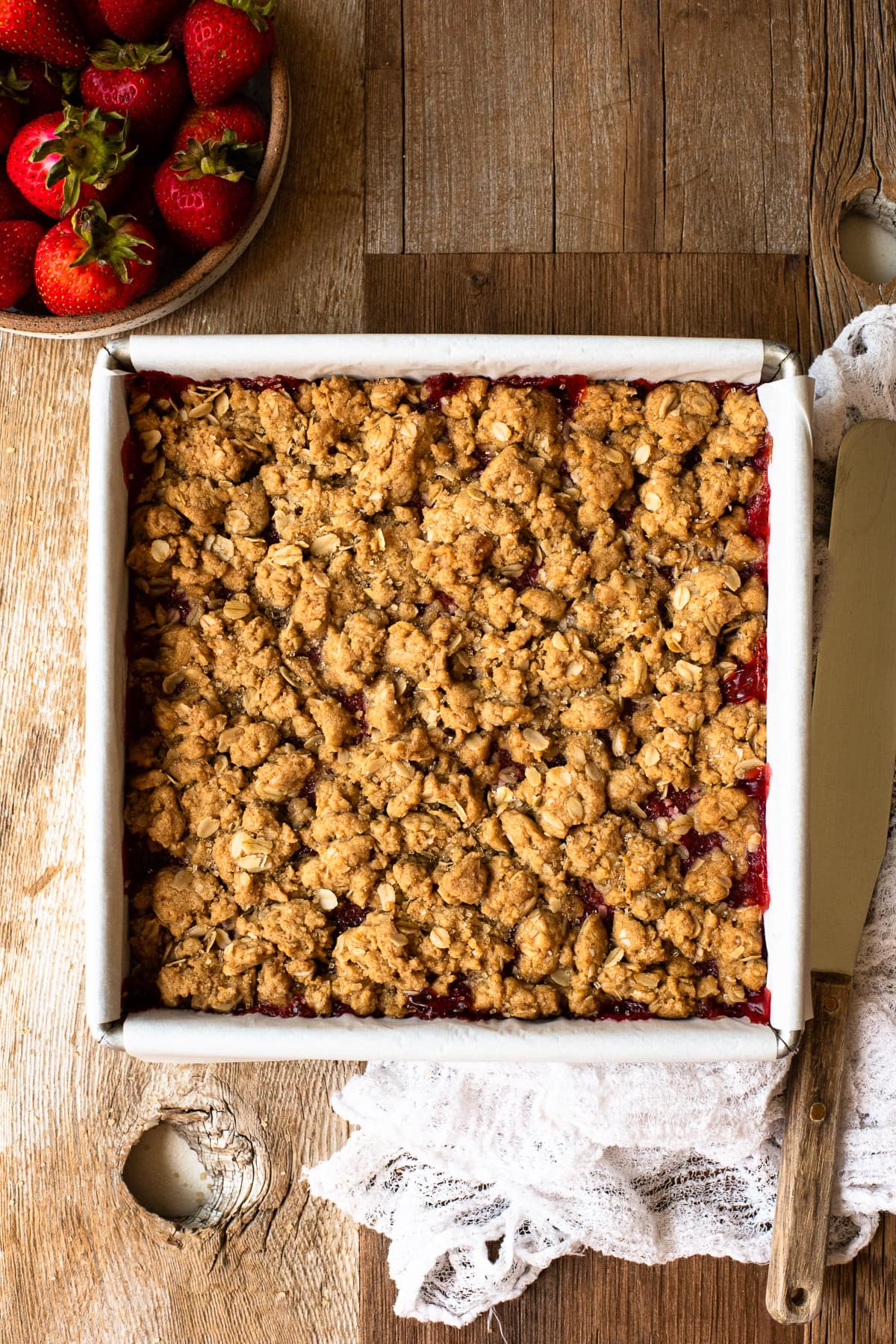 Strawberry crumb bars cooling in a parchment-lined pan.