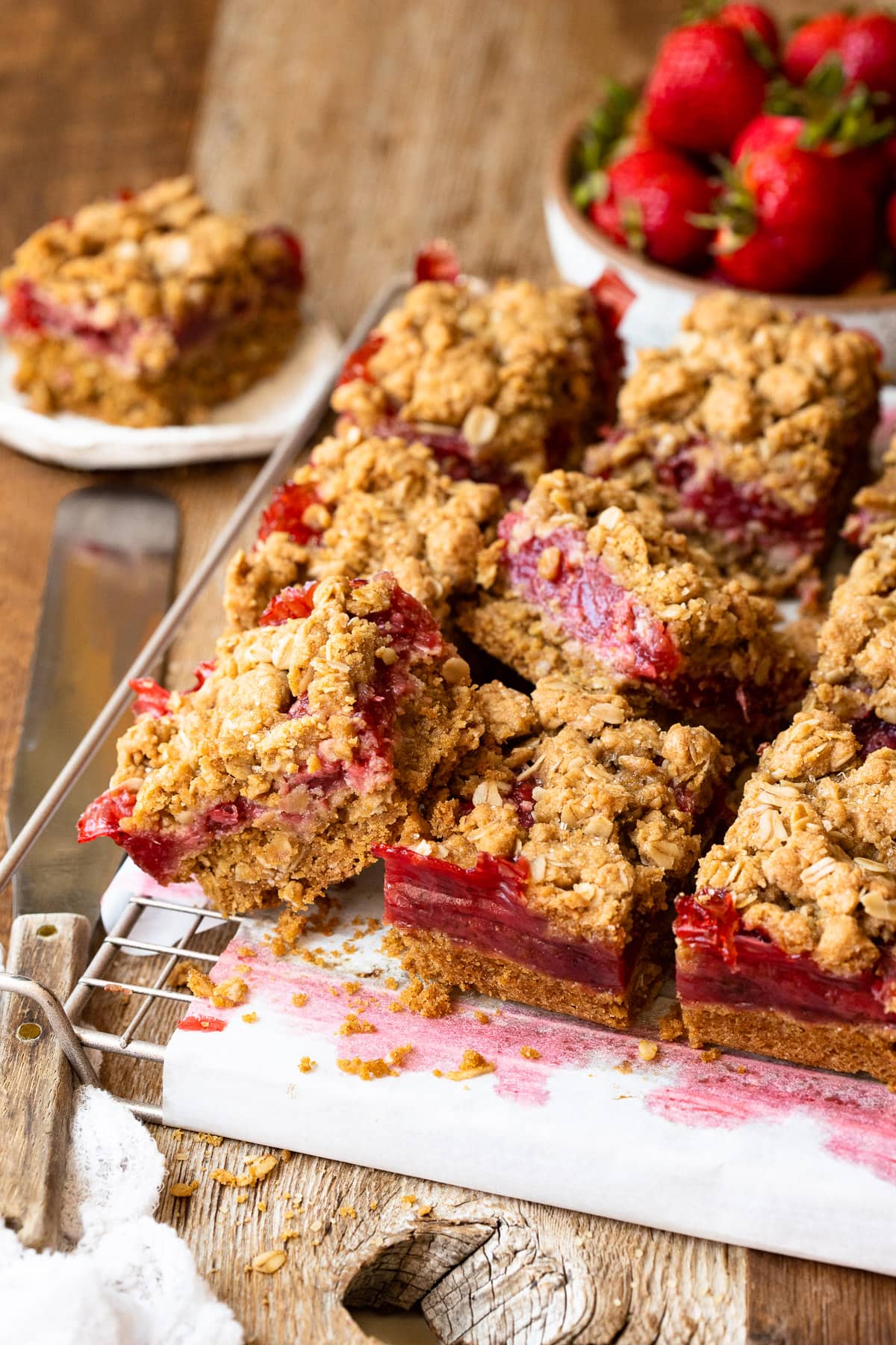 Strawberry oatmeal crumb bars sitting on a wire rack, with strawberries in the background.