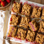 Strawberry bars on a parchment-lined wire rack, with a bowl of strawberries.