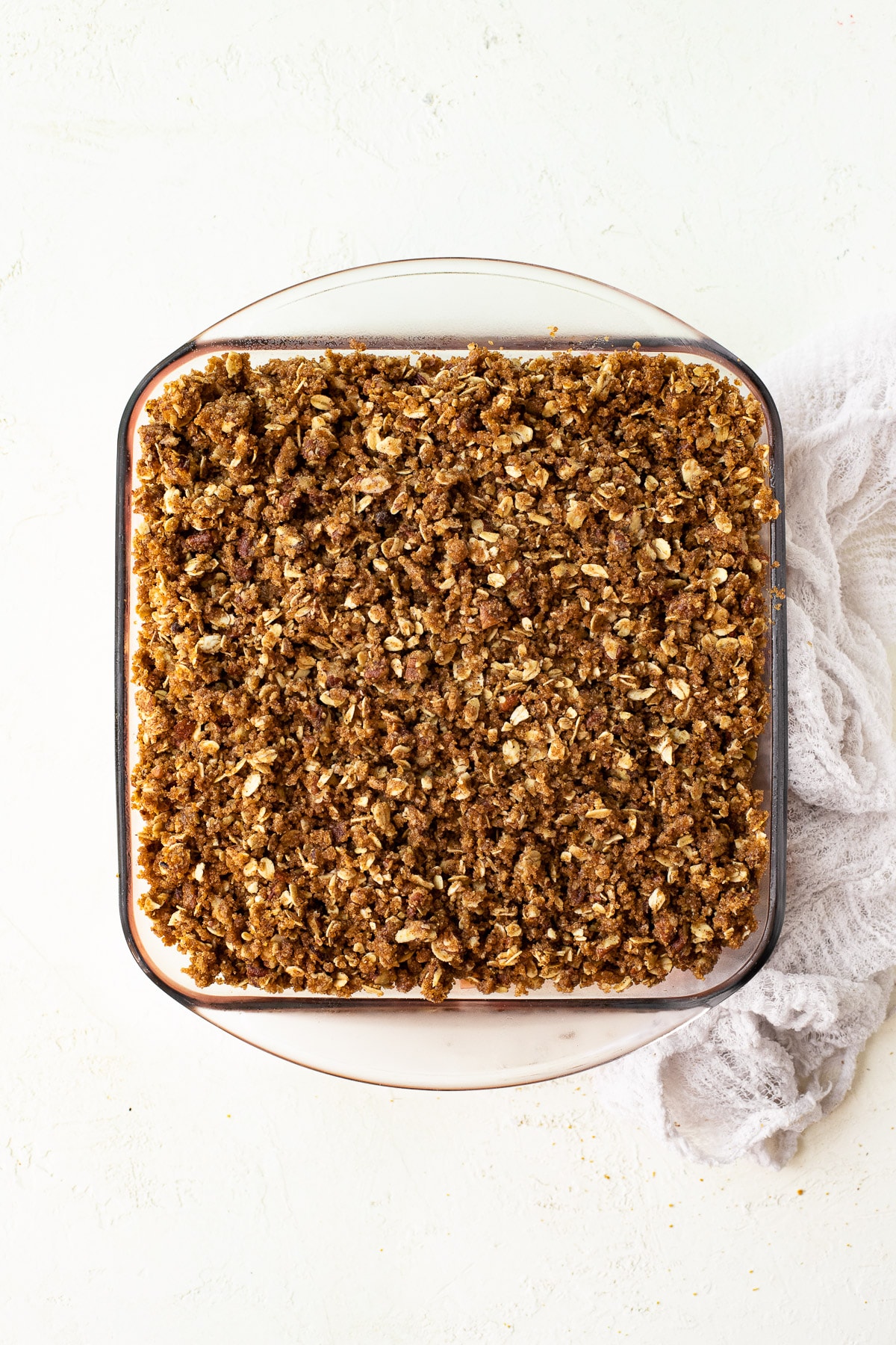 A square baking dish filled with fruit and covered with crumble topping.