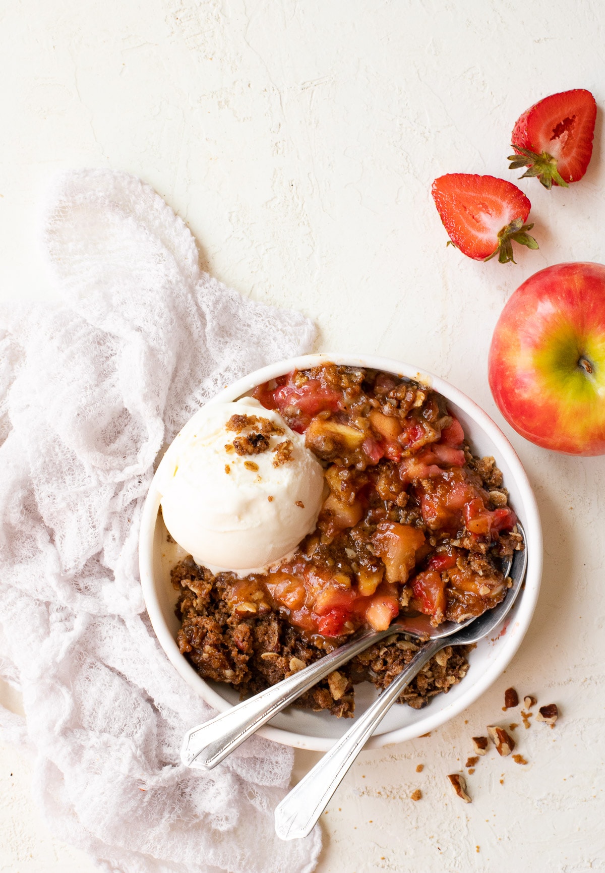 A serving of strawberry apple crumble on a plate with a scoop of ice cream and two spoons.