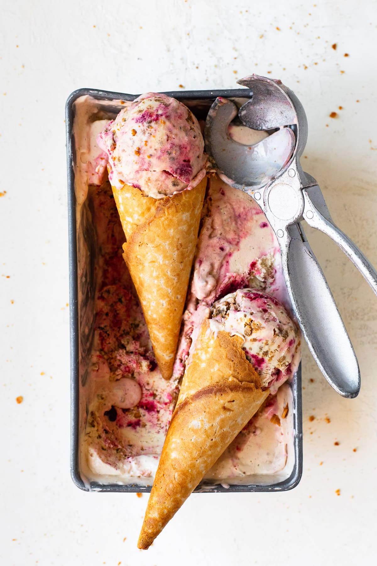 Berry cheesecake ice cream in waffle cones with an ice cream scoop.