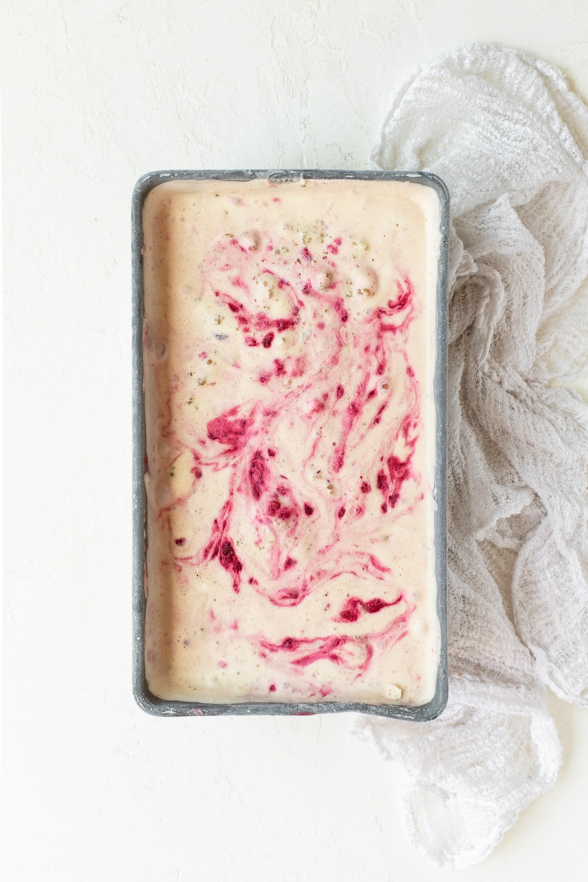 Berry-swirled cheesecake ice cream in a metal loaf pan with a white linen.