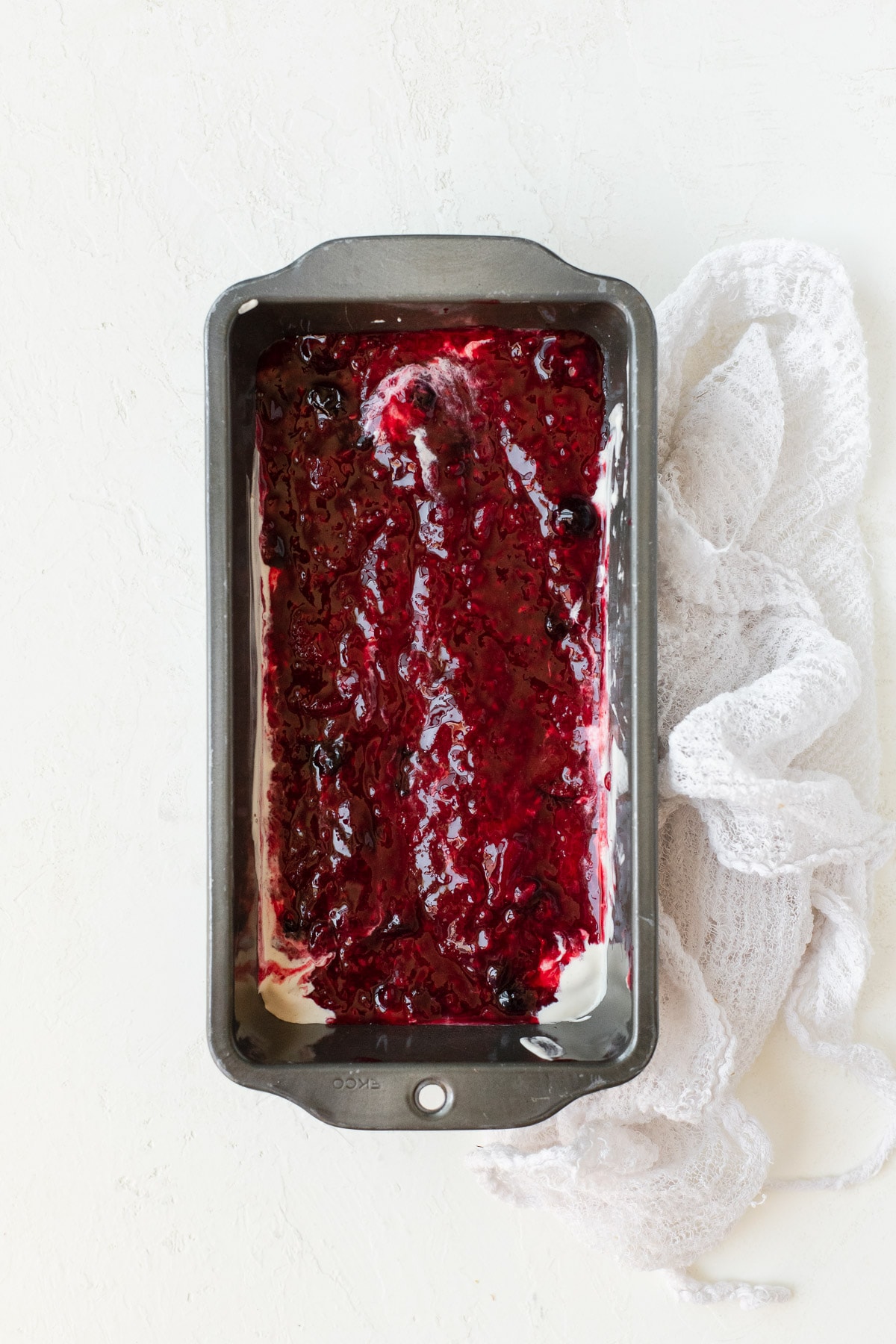 A layer of berry compote spread over ice cream in a metal loaf pan.